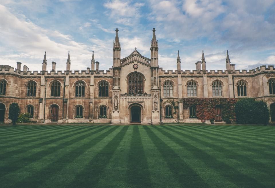 A historic university building with a striped lawn under a blue sky